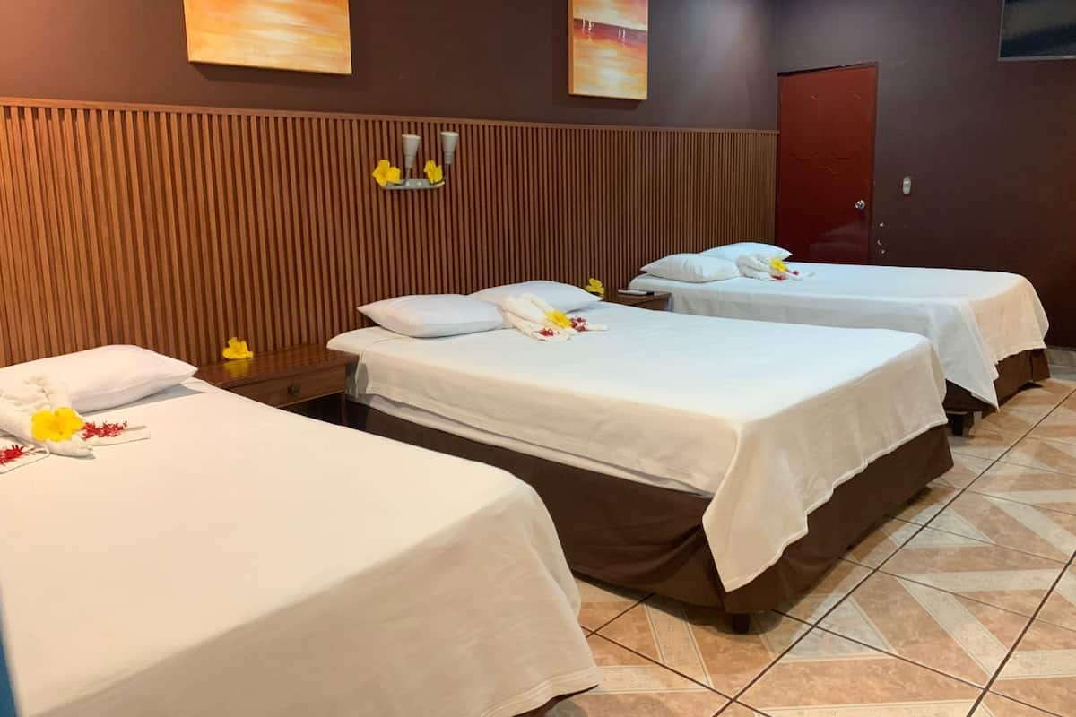 Hotellihuone, jossa on kolme sänkyä, seinät on verhoiltu puupaneelilla ja sänkyjen yläpuolella on taideteoksia.
