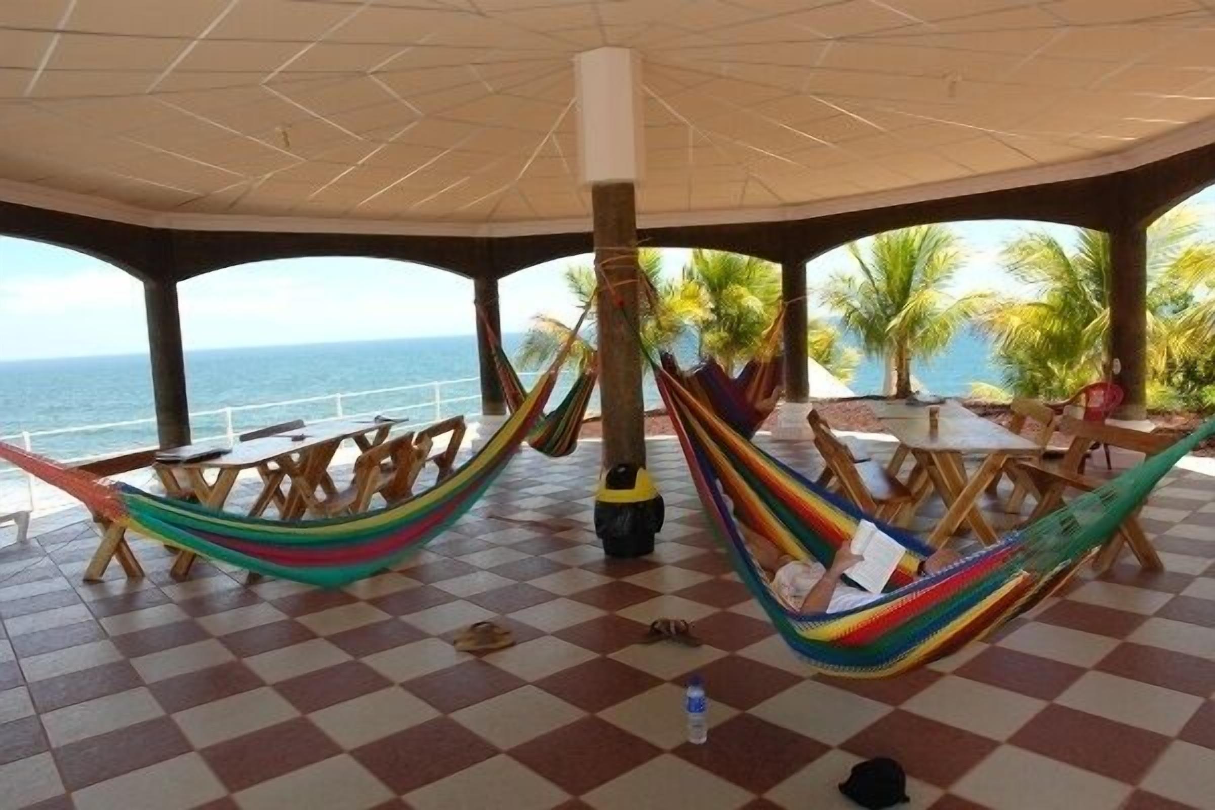 A covered outdoor seating area with hammocks, checkered flooring, and a view of the ocean.