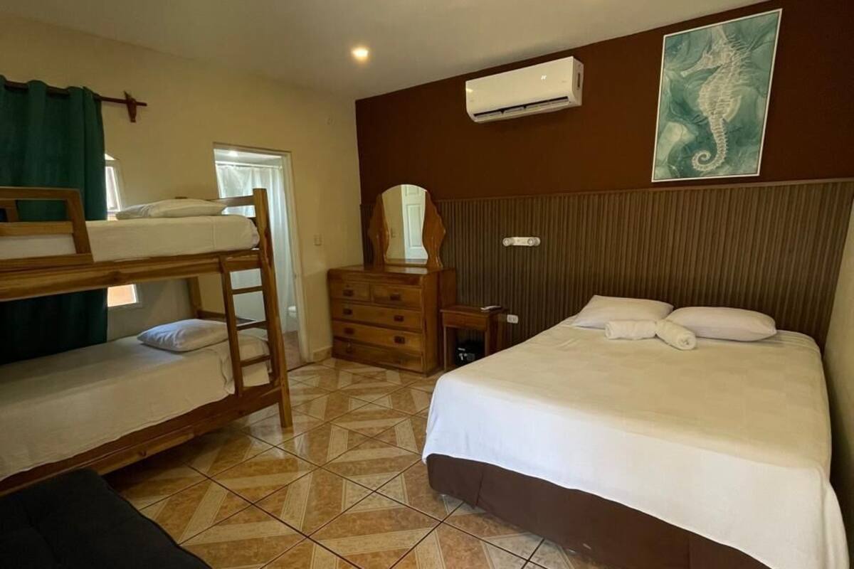 Een kamer met stapelbedden, een enkel bed, een kaptafel, een airconditioning en een schilderij aan de muur.