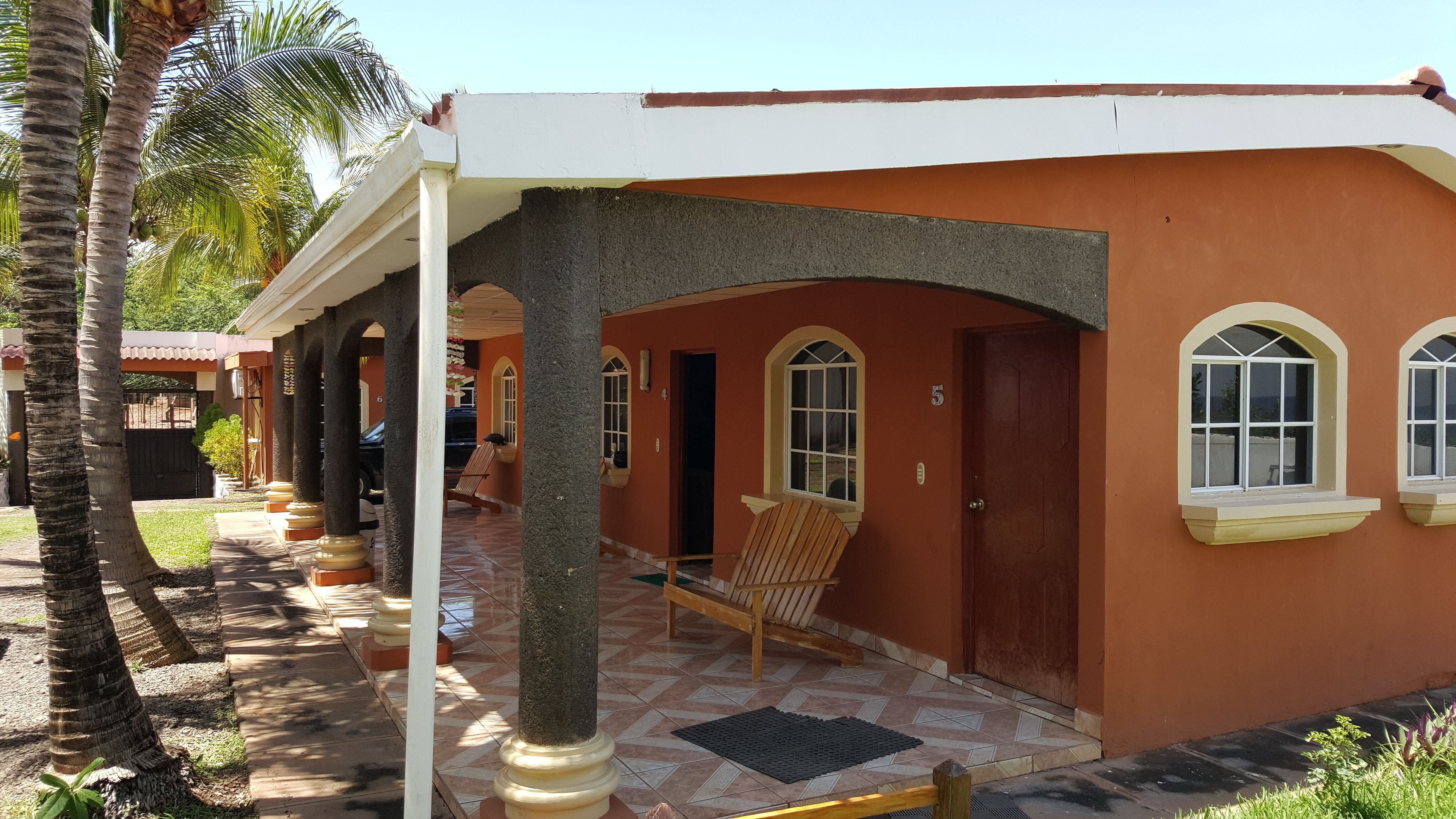 A two-story building with a covered porch, palm trees, and a tiled patio.