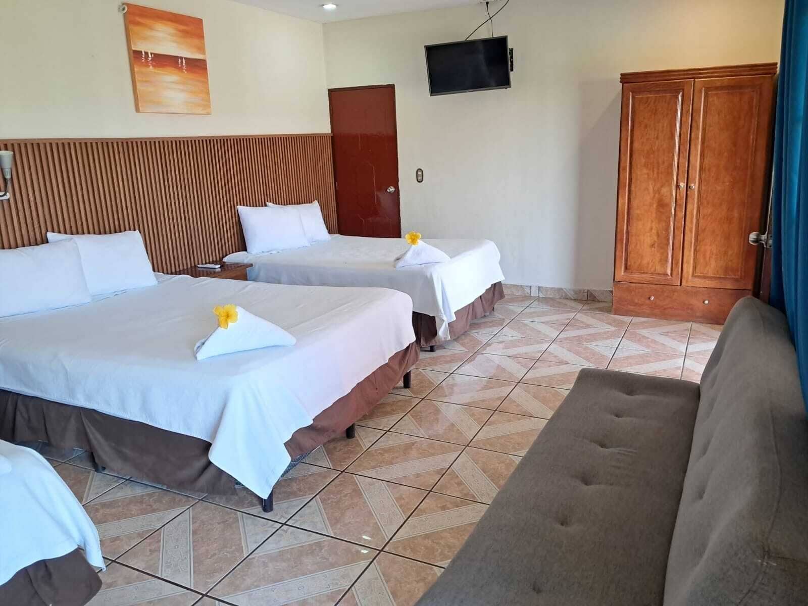A hotel room with two beds, a television, a wardrobe, and a sofa.