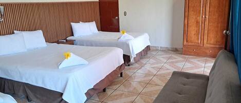 A hotel room with two beds, a television, a wardrobe, and a sofa.