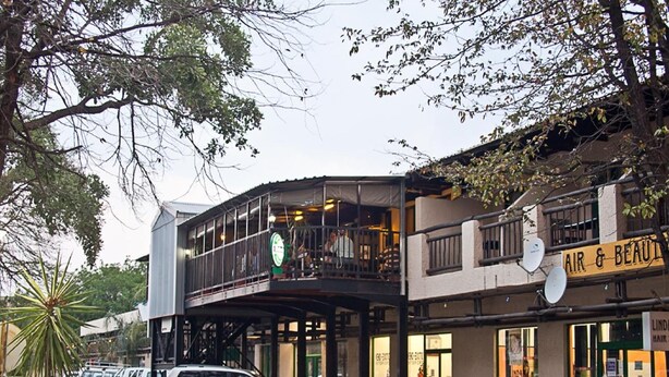 A street view with parked cars, a building with an 'AIR & BEAUTY' sign, and a balcony with a person visible. - Digger Inn (Francistown)