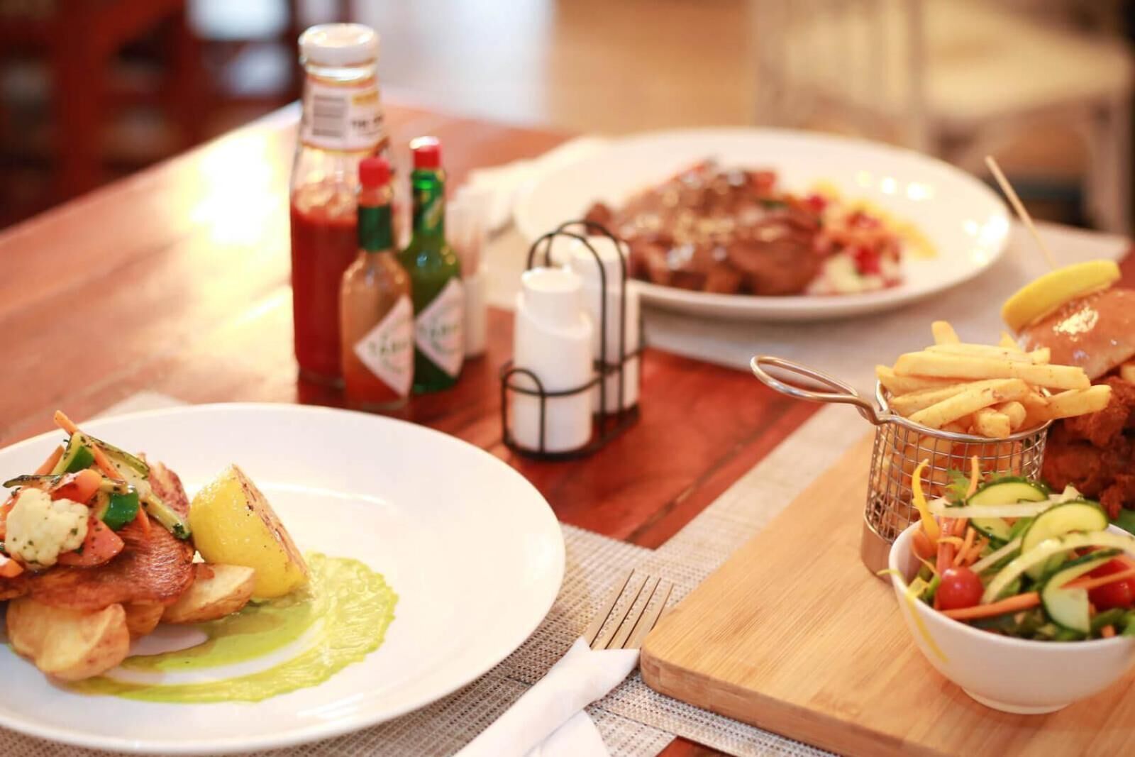 A wooden table with plates of food, including a salad, fries, and a meat dish.