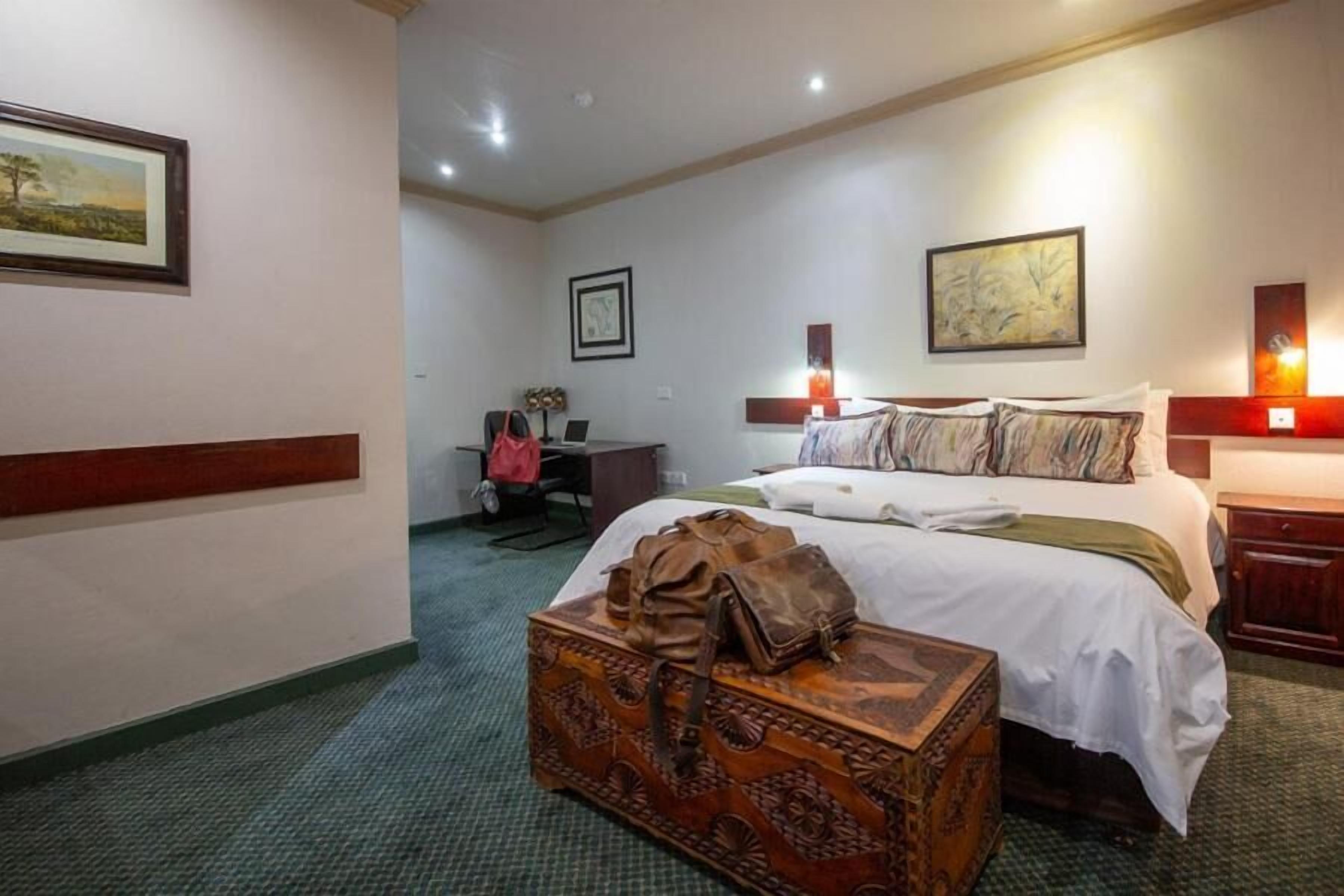 A hotel room with a large bed, a desk with a chair, a suitcase, and artwork on the walls.