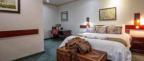 Una habitación de hotel con una cama grande, un escritorio con una silla, una maleta y obras de arte en las paredes.