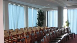 Een congreszaal met rijen houten stoelen en een grote potplant.