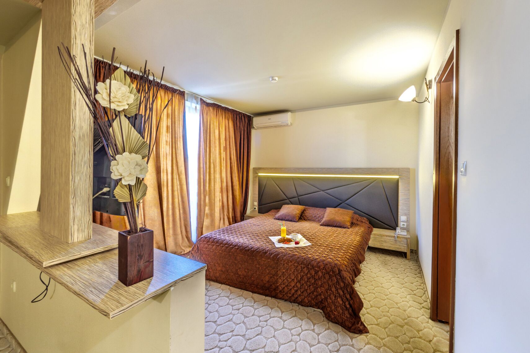 A hotel room with a bed, a nightstand, a bedside table, a mirror, and a window with curtains.