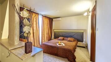 A hotel room with a bed, a nightstand, a bedside table, a mirror, and a window with curtains.