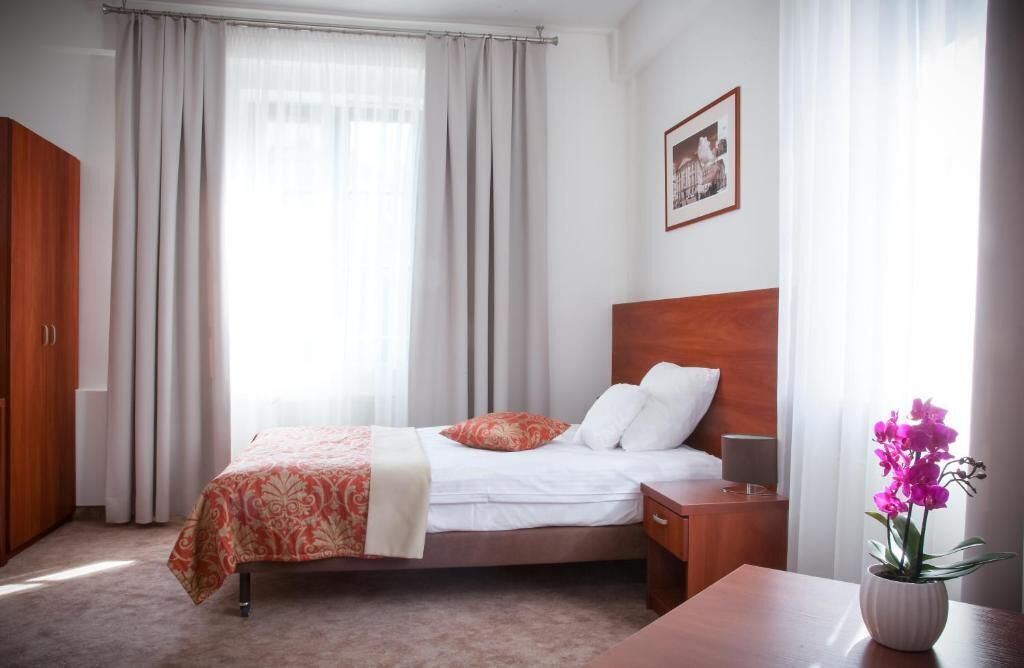 Habitación de hotel con cama, mesita de noche, armario de madera, ventana con cortinas e imagen enmarcadas en la pared.
