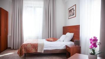 Habitación de hotel con cama, mesita de noche, armario de madera, ventana con cortinas e imagen enmarcadas en la pared.