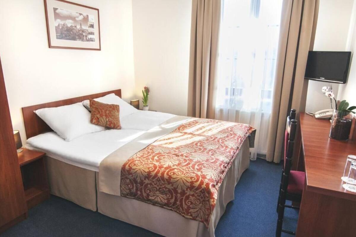 Una habitación de hotel con una cama, un escritorio con teléfono, un televisor y una ventana con cortinas.