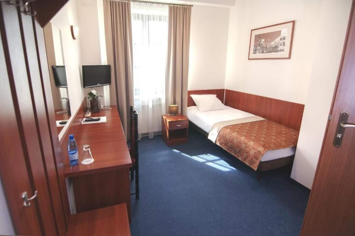 Habitación de hotel con cama, escritorio, silla, televisor, mesita de noche y ventana con cortinas.