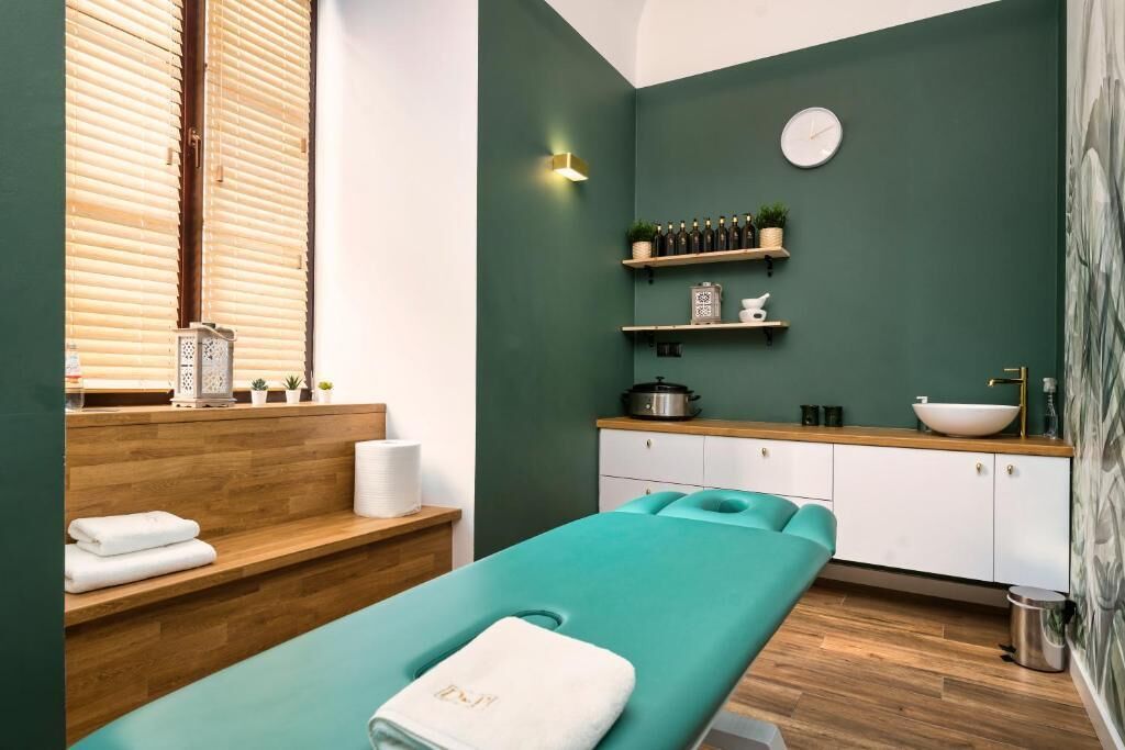 A spa room with a massage table, wooden shelves with bottles and plants, a sink, and a clock on the wall.