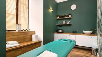 A spa room with a massage table, wooden shelves with bottles and plants, a sink, and a clock on the wall.