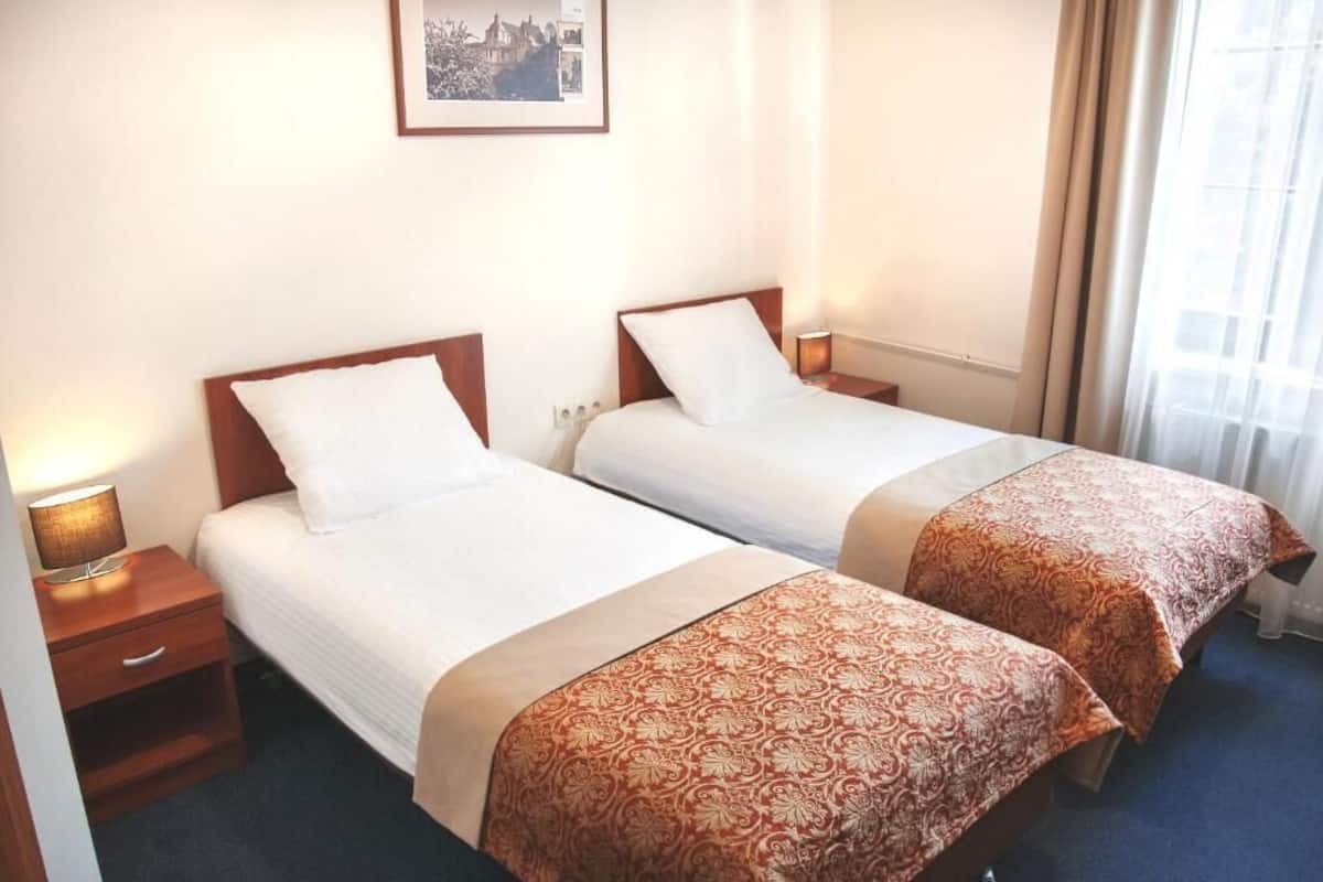 Habitación de hotel con dos camas individuales, cabeceros de madera, lámparas de noche, un cuadro en la pared y una ventana con cortinas.