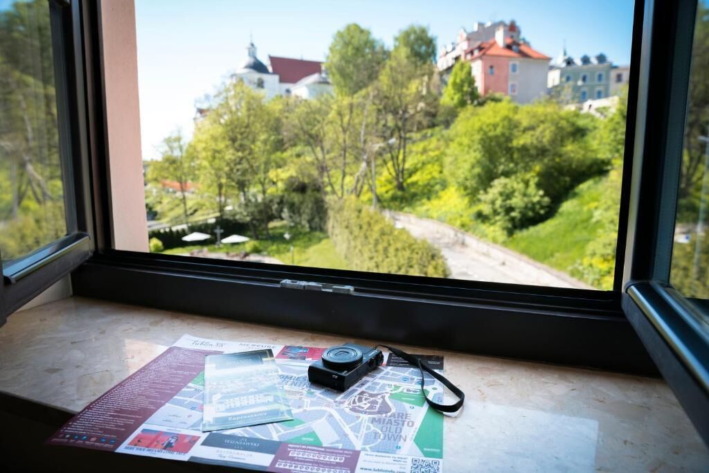 A window with a view of a green landscape and buildings, a map, and a camera on the sill.
