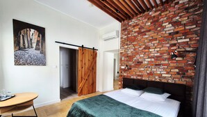 A bedroom with a brick wall, a bed with a green quilt, a wooden door, and a painting on the wall. - Dom Na Podwalu Lublin  (Lublin)