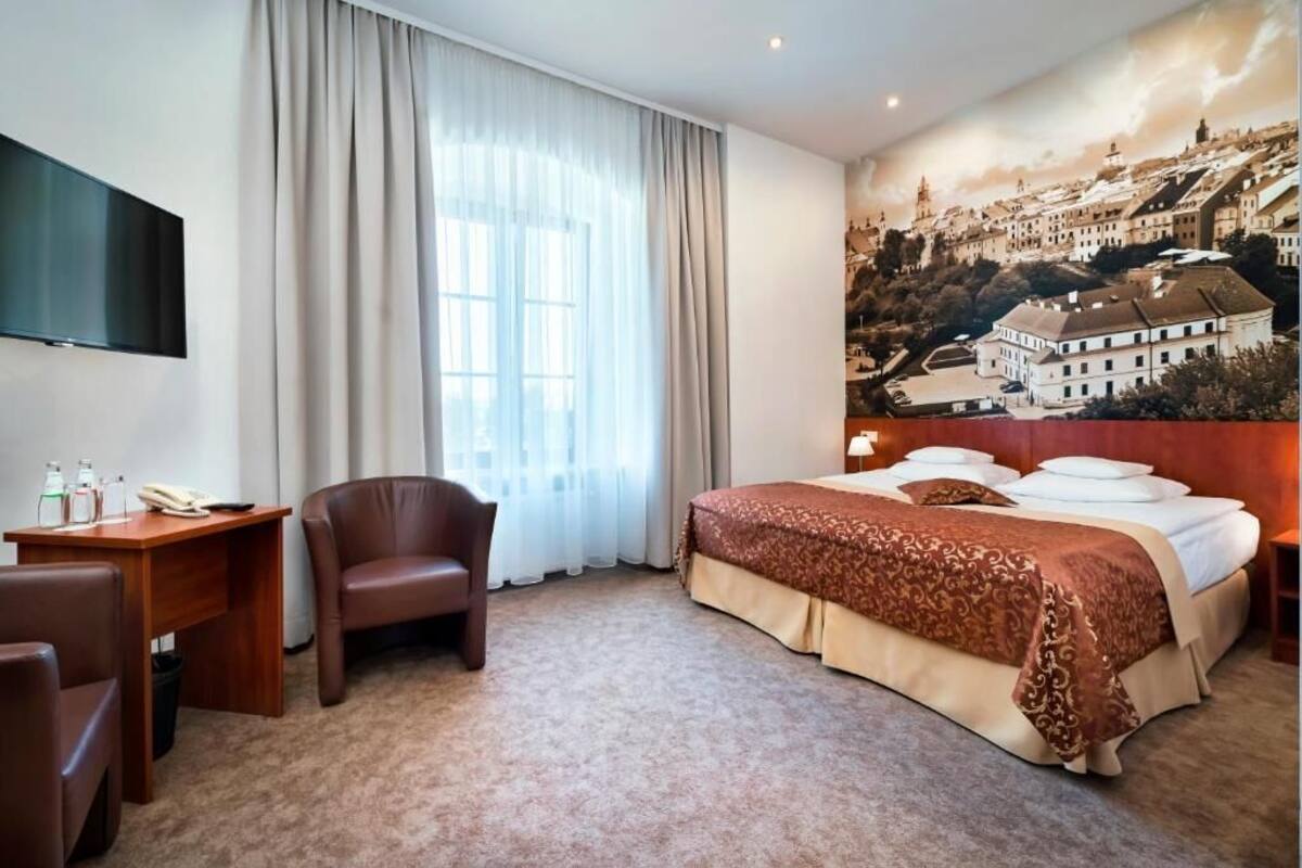 Una habitación de hotel con cama, escritorio, silla, televisión y un ventanal con cortinas.