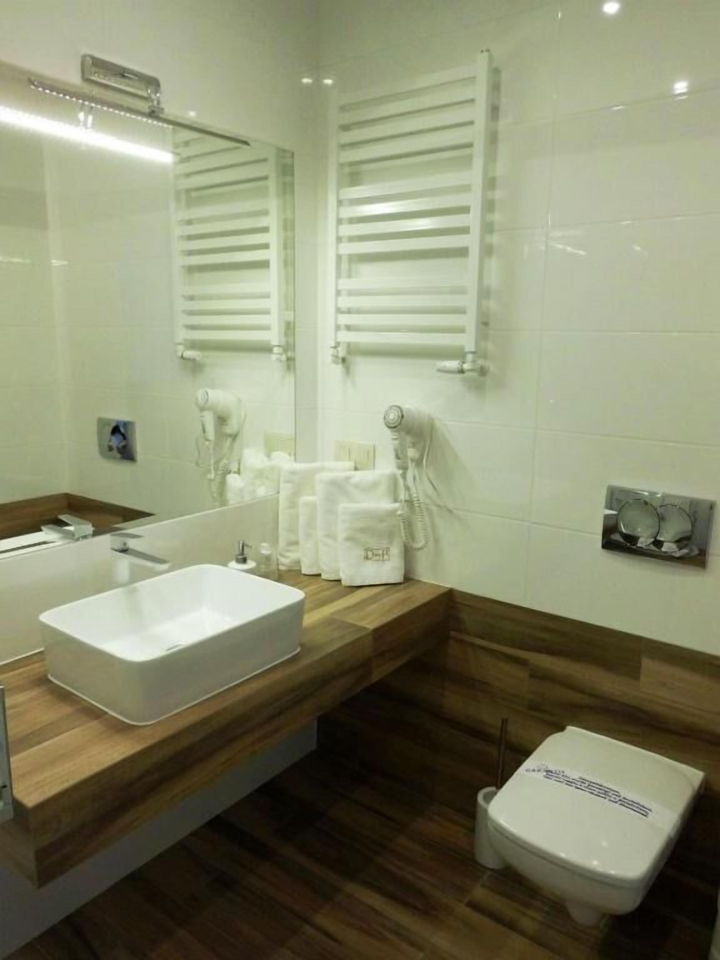 A modern bathroom with a large mirror, a white sink, a wooden vanity, and a toilet.