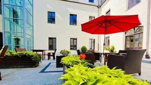 An outdoor seating area with tables and chairs, a red umbrella, and green plants. - Dom Na Podwalu Lublin  (Lublin)