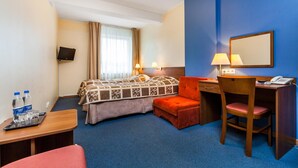 A hotel room with a bed, desk, chair, and a small table with a lamp. - Hotel Olivia (Gdańsk)