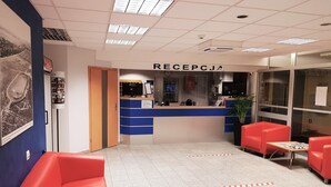 A reception area with a blue counter, red seating, and a framed picture on the wall. - Hotel Olivia (Gdańsk)