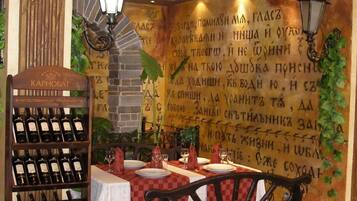 Interior de restaurante con una estantería de vinos, mesas, sillas y una pared con texto escrito a mano.