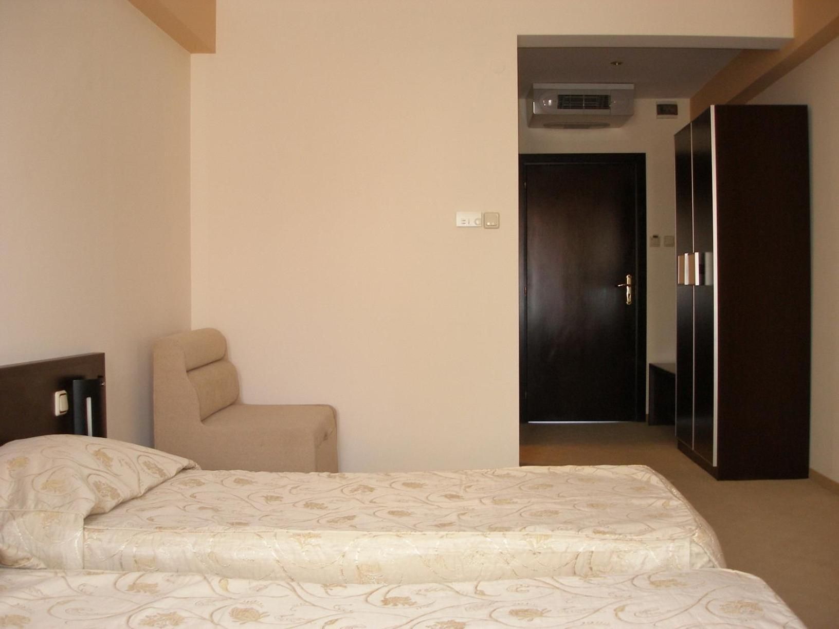 A hotel room with a bed, a chair, a wardrobe, and a door leading to another room.