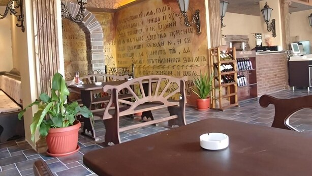 Interior de restaurante con pared de piedra, mobiliario de madera y suelo de baldosas.