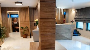 A modern interior with a marble floor, wooden accents, a reception desk, and a potted plant.