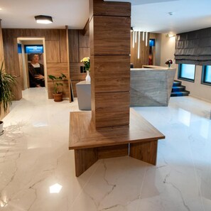 Un interior modern amb sòl de marbre, detalls de fusta, una recepció i una planta en test.