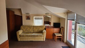 A small, cozy living area with a sofa, a chair, a desk with a television, and a window with blinds.