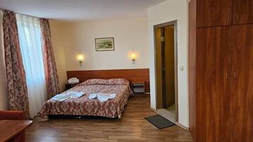 Habitación de hotel con una cama de madera, dos lámparas de noche, un armario de madera y una puerta que da a un balcón.