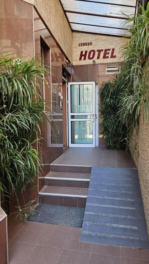 Ingresso di un hotel con porta in vetro, gradini d'accesso e piante in vaso su entrambi i lati.