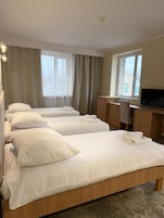 Habitación de hotel con tres camas, un escritorio y un televisor.