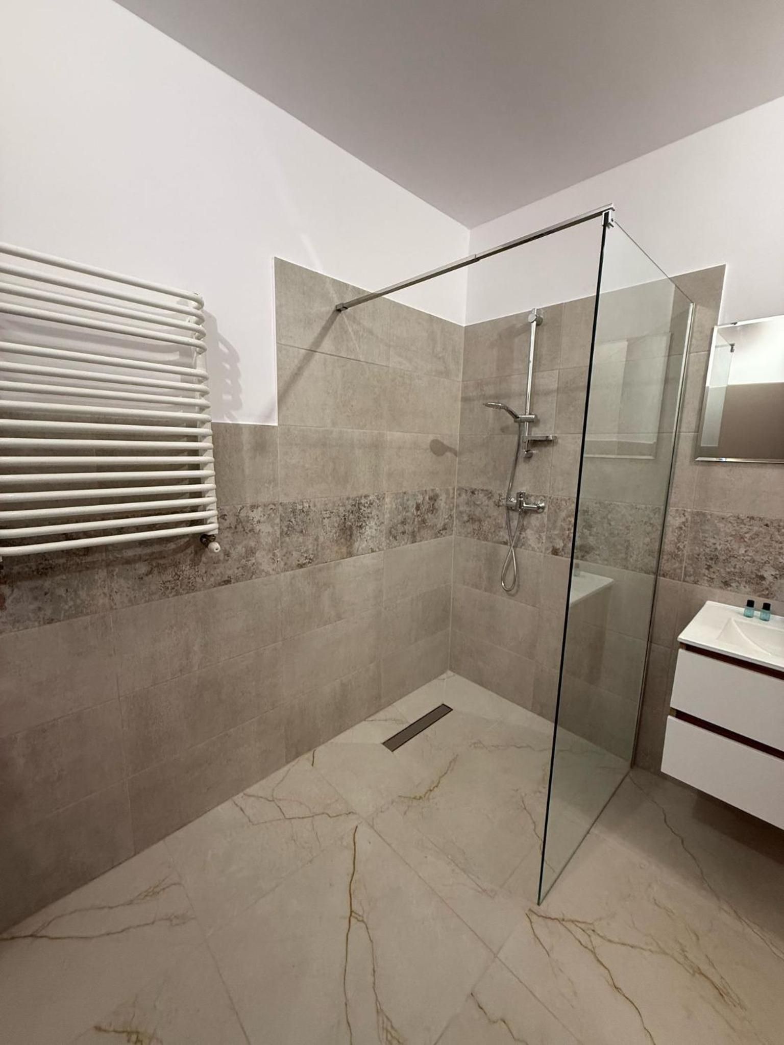A modern bathroom with a glass shower enclosure, a white sink, and a towel rack.