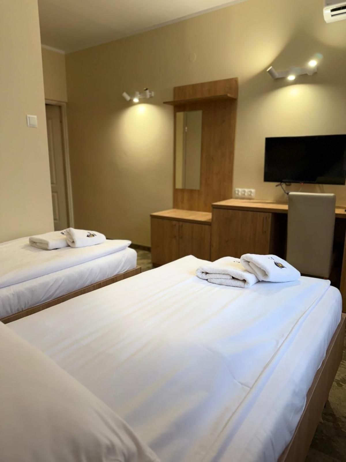 A hotel room with two beds, a desk, a flat-screen TV, and a mirror.