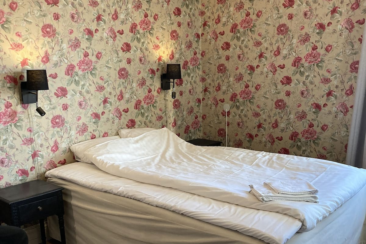 Ein Schlafzimmer mit einem großen Bett, floralem Wandpapier, zwei Wandleuchten und einem Holzboden.