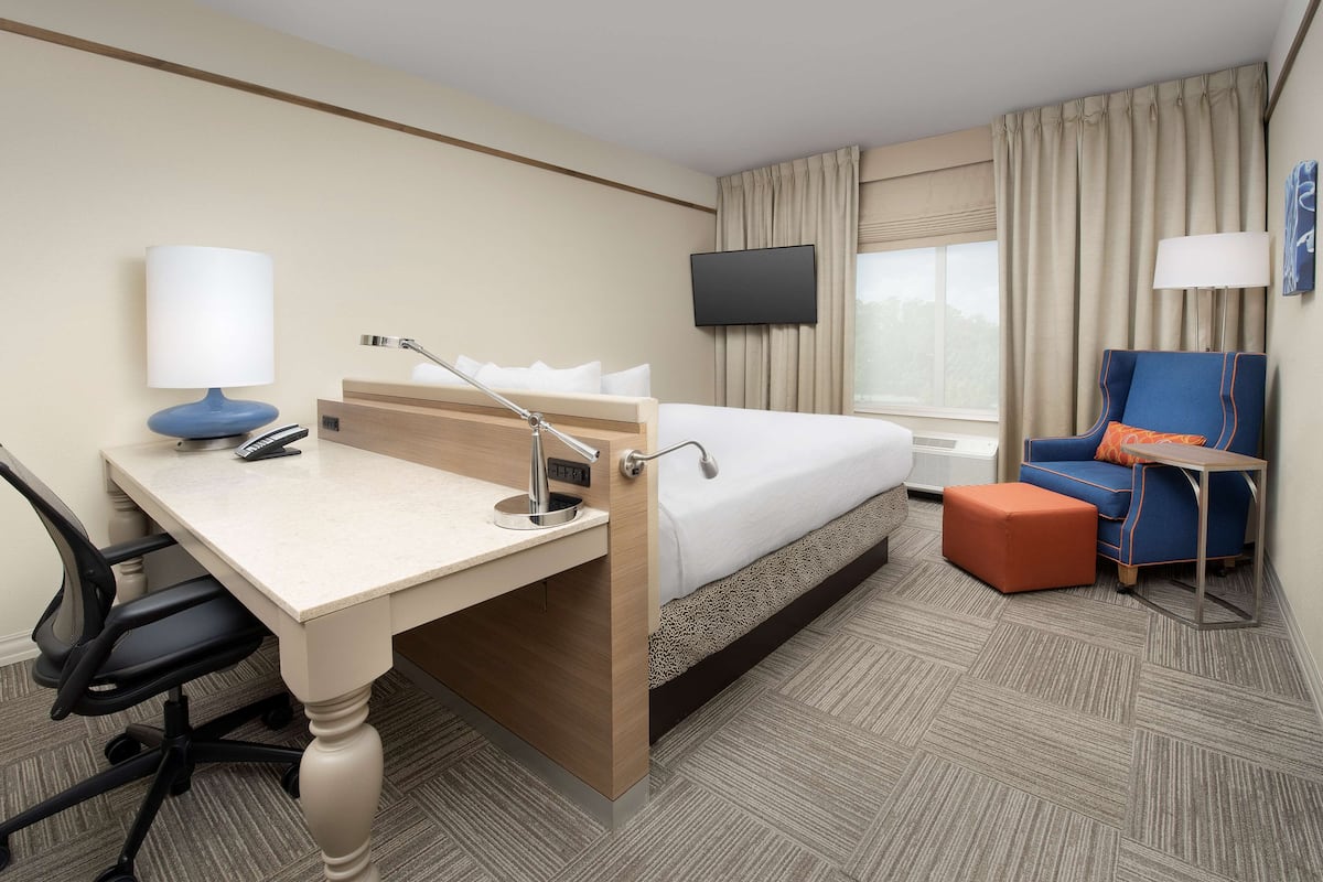 A hotel room with a bed, desk, chair, TV, and a small table.