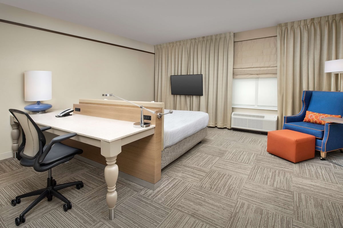A hotel room with a bed, desk, chair, TV, and a window with curtains.