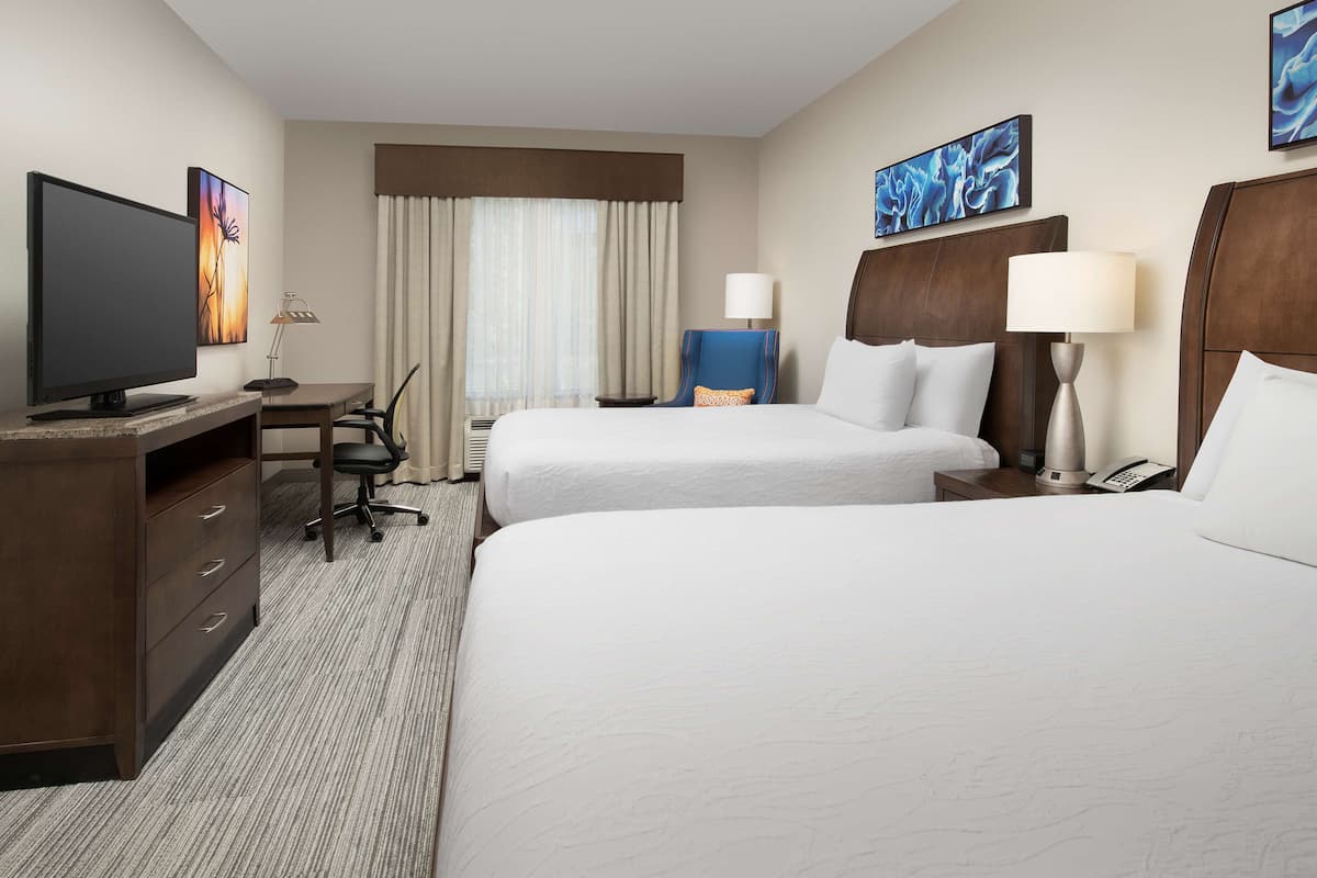 A hotel room with two beds, a desk, a television, and a chair.