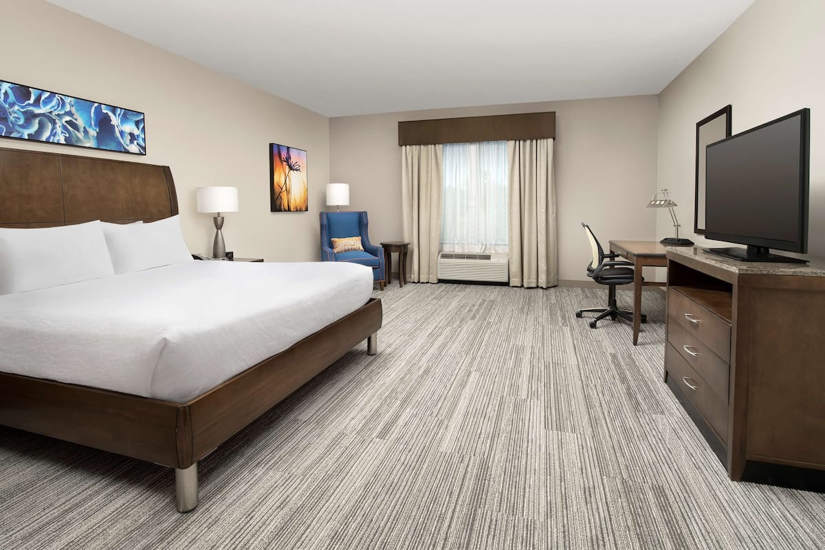 A hotel room with a large bed, a desk with a computer, a chair, and a TV.