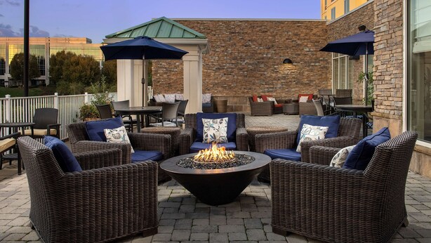 A patio area with wicker furniture, a central fire pit, and outdoor umbrellas.