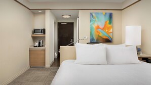 A hotel room with a bed, a microwave, a coffee maker, a painting, and a lamp.