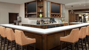 A bar area with a long counter, multiple stools, and a variety of bottles and glasses.
