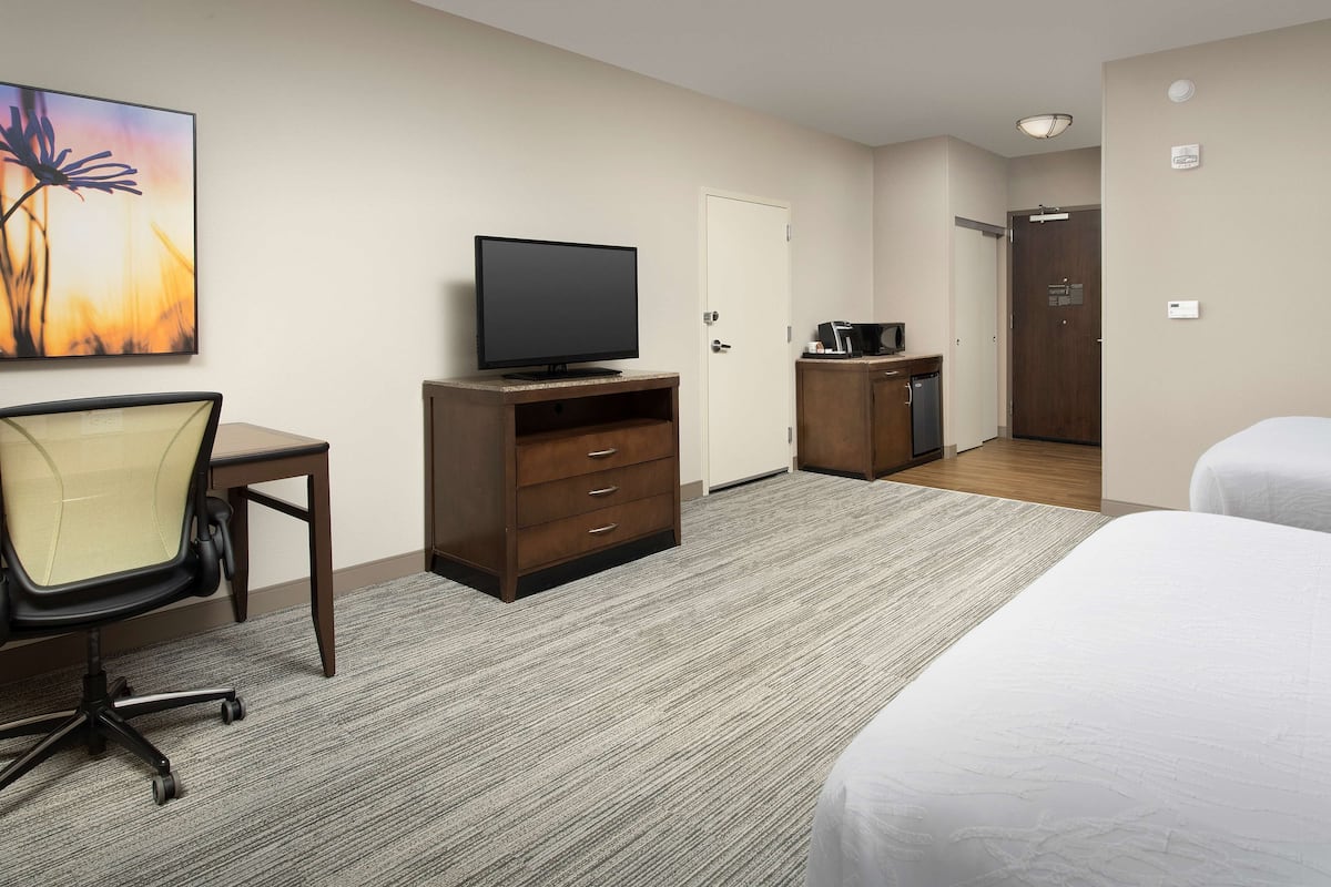 A hotel room with a bed, a desk with a chair, a television, a wardrobe, and a door leading to another room.