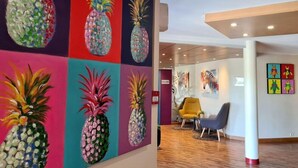 A hallway with a colorful pineapple mural on the wall, wooden flooring, and modern chairs.