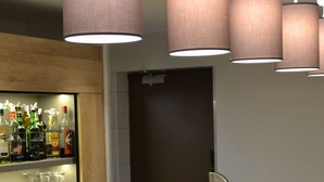 A bar area with a counter, shelves with bottles, and hanging lamps.