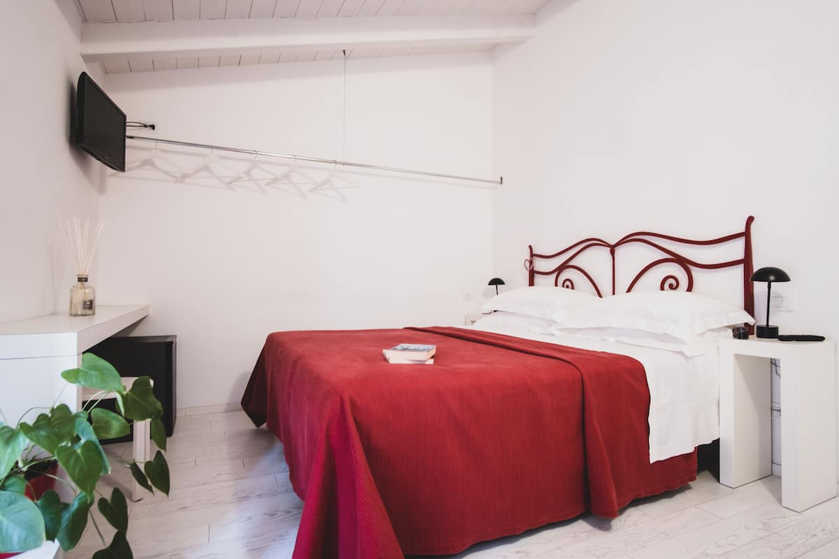 A bedroom with a bed, bedside table, lamp, and a TV mounted on the wall.